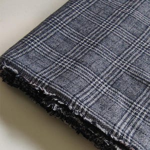 Puede incluir: Una pieza de tela doblada con un patr&oacute;n de cuadros en azul marino oscuro y blanco. El tejido tiene una textura visible y un borde deshilachado y sin rematar a lo largo del pliegue inferior, mostrando la construcci&oacute;n del material.