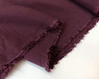 May include: A length of deep plum-colored fabric with a smooth, matte texture. The material features raw, frayed edges along the cut sides, showing loose threads and a slightly uneven finish. The fabric is folded over itself, creating soft drapes.