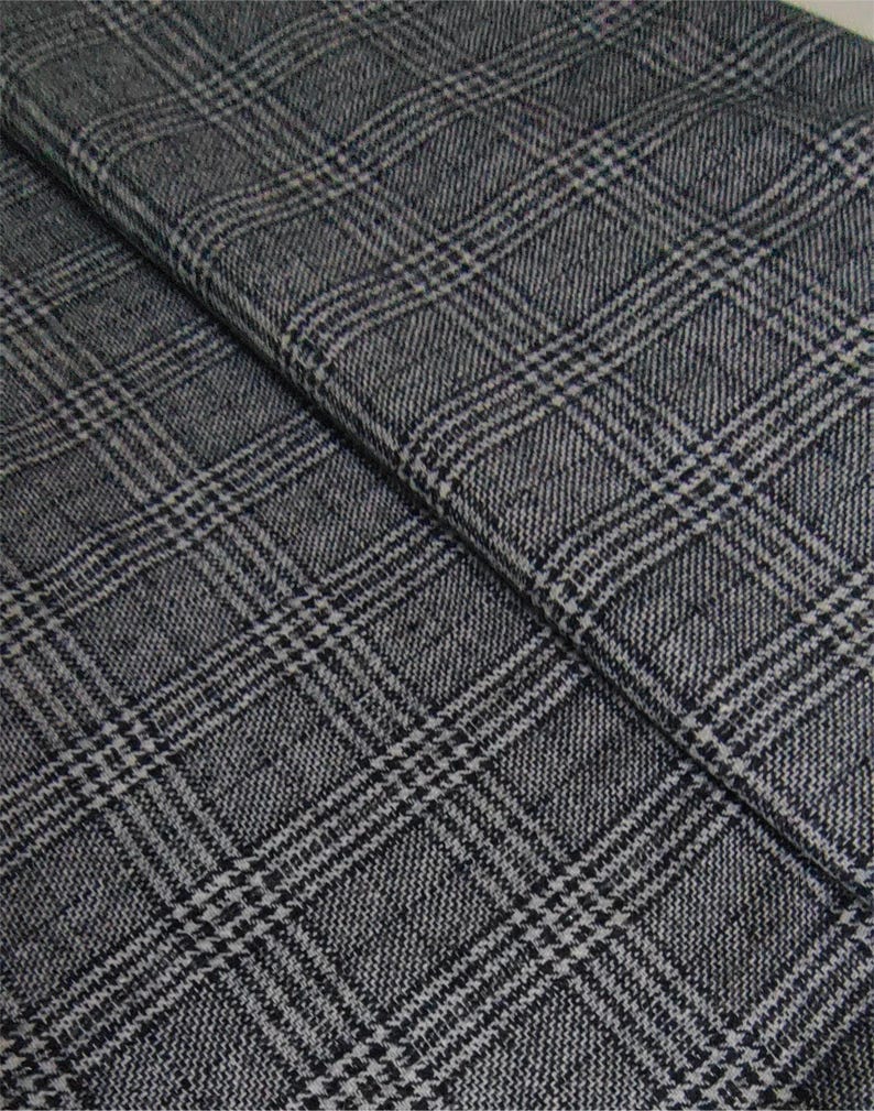 Puede incluir: Una pieza de tela doblada con un patr&oacute;n de cuadros en gris oscuro y negro. El tejido muestra una textura tejida con un dise&ntilde;o de cuadr&iacute;cula repetitivo compuesto por l&iacute;neas horizontales y verticales que se cruzan, creando un aspecto cl&aacute;sico.