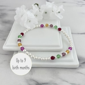 May include: A beaded bracelet featuring small, polished silver-tone spheres interspersed with multi-coloured faceted crystal beads in shades of red, green, purple, and yellow. A circular white graphic overlay displays the text Up to 9 birth months.