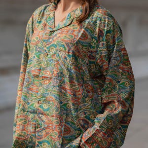 May include: A long-sleeved paisley print shirt and matching pants in shades of green, red, and gold. The shirt has a collared neckline and button-down front. The fabric has a detailed, swirling pattern.