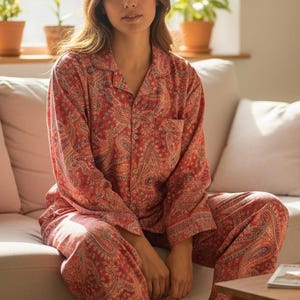 Puede incluir: Conjunto de pijama de cachemira rojo. El conjunto de dos piezas incluye una camisa con botones y bolsillo en el pecho y pantalones a juego. El pijama tiene un estampado de cachemira clásico en tonos rojos, azules y blancos.