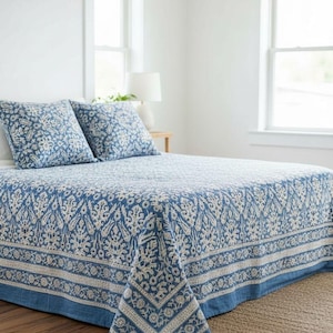 Könnte beinhalten: Ein blau-weiß gemusterter Bettüberwurf und zwei passende Kissenbezüge auf einem Bett. Die Bettwäsche weist ein detailliertes Blumendesign auf. Der Raum hat weiße Wände und Fenster mit einem neutralfarbenen Teppich auf dem Boden.