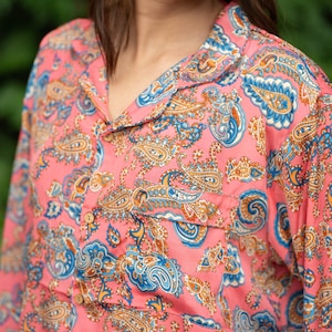 May include: Pink paisley print shirt with a collared neckline and a chest pocket. The shirt features a vibrant pattern in shades of blue, orange, and white. The long-sleeved shirt is made of a soft, lightweight fabric.