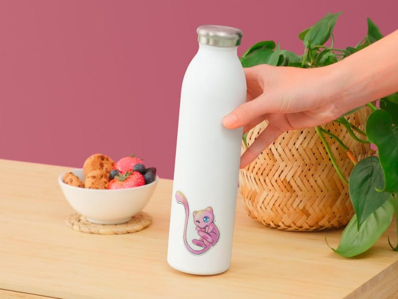 May include: A white cylindrical water bottle with a metallic silver cap, featuring a small, colorful sticker of a pink, cat-like creature with a long tail and blue eyes positioned on the lower front section of the bottle's smooth exterior surface.