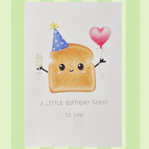 May include: A white greeting card featuring a cartoon slice of golden brown toast wearing a blue polka-dot party hat. The toast holds a champagne flute and a pink heart-shaped balloon. The text reads: A LITTLE BIRTHDAY TOAST TO YOU.