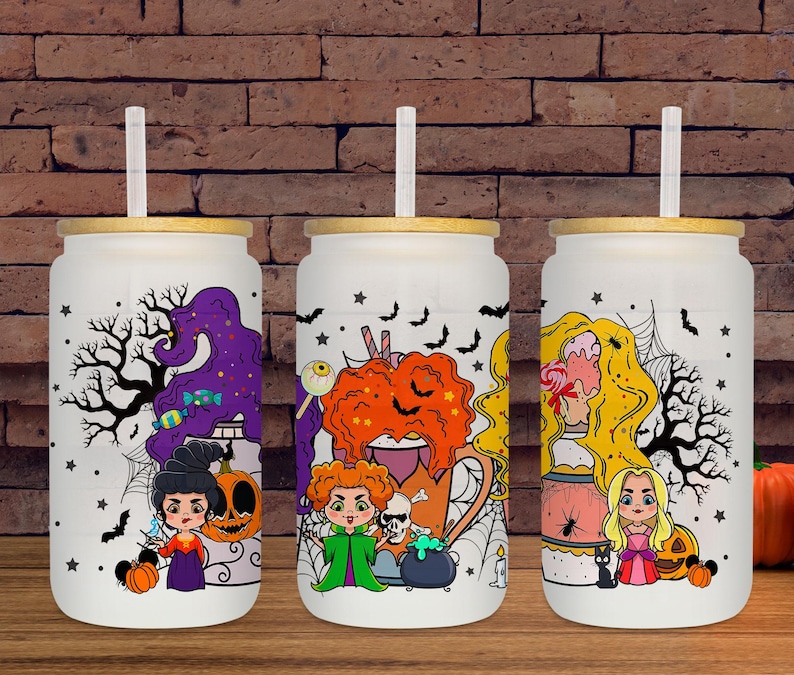 May include: Three white glass tumblers with bamboo lids and straws, each featuring a Halloween-themed design. The designs include cartoon witches, pumpkins, bats, and spiderwebs. The tumblers are set against a brick background.