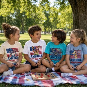 May include: Four children sitting on a picnic blanket, wearing t-shirts with patriotic animal designs and the word "AMERICA". The shirts feature a rabbit, fox, bull, and goat with sunglasses, set against a flag background. A checkerboard is in front of them.