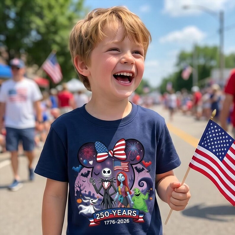 May include: A navy blue short-sleeve t-shirt featuring a graphic of Jack Skellington, Sally, and Zero from The Nightmare Before Christmas, a Mickey Mouse silhouette, fireworks, and the text 250-YEARS 1776-2026 with an American flag motif.
