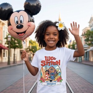 Op de afbeelding: Een jong persoon draagt een wit t-shirt met een kleurrijke "Lilo & Stitch" afbeelding en een Mickey Mouse ballon. Het shirt toont de personages Lilo, Stitch en anderen, met de tekst "Disneyland" eronder. Een bloem zit in hun haar.