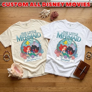 May include: Two t-shirts featuring "The Little Mermaid" graphic. One is cream-colored, the other white. The design includes Ariel, Flounder, and Ursula. The text "CUSTOM ALL DISNEY MOVIES" is at the top. One shirt says "Walt Disney World" and the other says "Disneyland".