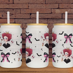May include: Three white glass tumblers with bamboo lids and straws. Each tumbler features a design of a queen with a red curly hairstyle, playing cards, bats, and bows. The tumblers are on a wooden surface.