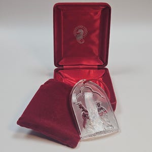 May include: A clear crystal Christmas ornament with the year 1999 etched on it, depicting three figures. The ornament is displayed with a red velvet box and pouch. The Waterford Crystal logo is visible on the box.
