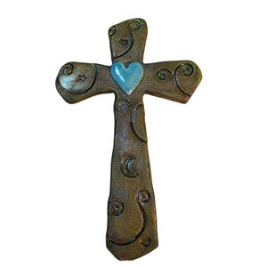 May include: A decorative wall cross made of dark, textured bronze-toned material. The surface features etched swirl patterns, a small star, and a crescent moon. A smooth, light blue ceramic heart is centered at the intersection of the cross arms.