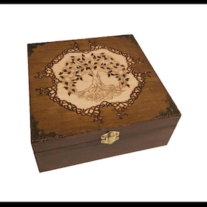 Op de afbeelding: Een houten doos met een scharnierend deksel en een messing sluiting. De bovenkant van de doos is versierd met een ingebrand ontwerp van een Keltische levensboom.