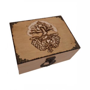 Può includere: Una scatola di legno con un coperchio incernierato e una chiusura in metallo. La scatola è decorata con un disegno di albero della vita bruciato a legno con dettagli intricati.