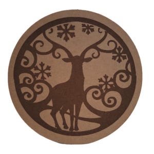 May include: A brown circular coaster with a laser-cut design of a deer with antlers standing in a winter scene with snowflakes and swirls.