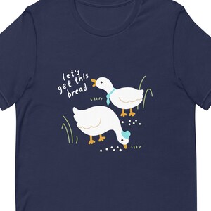 May include: A navy blue t-shirt featuring a white goose design and the text "Let's get this bread".