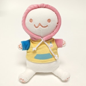 May include: A plush doll with a white body, wearing a pink hooded sweatshirt and a yellow shirt with a blue pocket. The doll has embroidered facial features and small, rounded feet. The doll's arms are blue and pink.