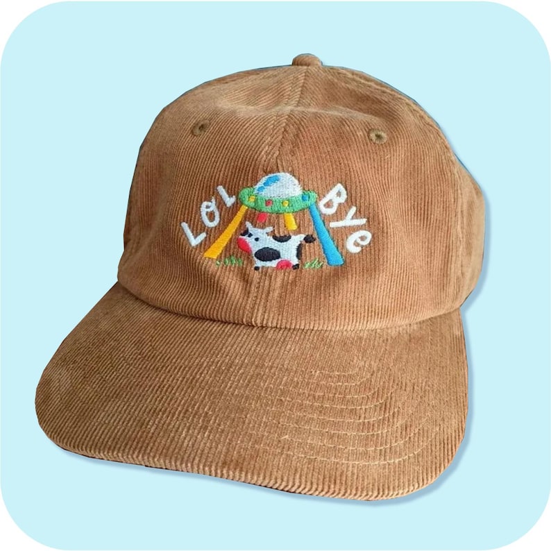 May include: A brown corduroy baseball cap with an embroidered design of a cow being abducted by a UFO. The text "LOL BYE" is embroidered on the cap.