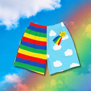 May include: Athletic shorts featuring a split design. The left side has horizontal stripes in red, yellow, blue, and green. The right side is light blue with white clouds and a yellow star graphic with the text "You're doing GREAT!" and a rainbow tail.