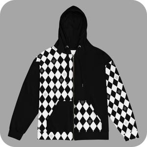 Peut inclure: Sweat à capuche noir et blanc à fermeture éclair avec une capuche noire. Le sweat à capuche a un motif en losanges avec de petites couronnes grises sur les losanges.