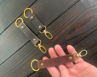 May include: Three leather keychains with gold metal rings and clasps. Two keychains are brown and one is dark brown.