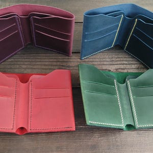 Puede incluir: Cuatro carteras de cuero abiertas en colores burdeos, azul, rojo y verde. Cada cartera tiene múltiples ranuras para tarjetas y un compartimento para billetes. Las carteras se exhiben sobre una superficie de madera oscura.