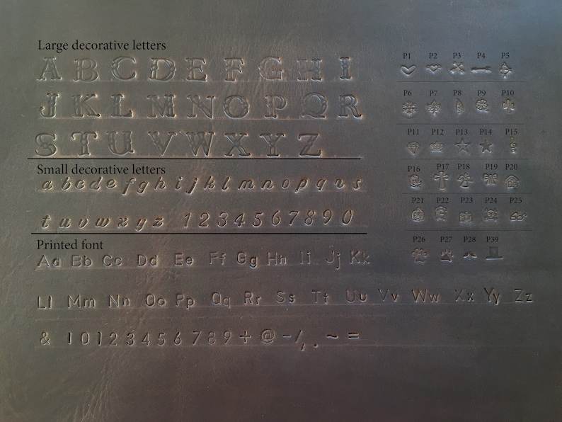 May include: A gray metal surface with embossed lettering and symbols. The image displays large and small decorative letters, a printed font, numbers, and various symbols, including hearts, stars, and crosses.