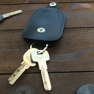 May include: A black leather key holder with a snap closure and a silver key ring. Two keys are attached to the ring, one with the word "Turcia" and the other with the word "Apecs".