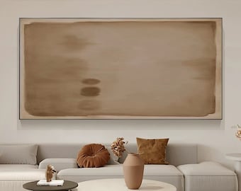 May include: A large abstract painting in shades of brown hangs above a white sofa with brown throw pillows. A vase with a brown glaze sits on a white coffee table with a brown base.