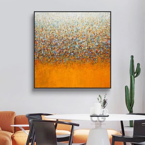 Puede incluir: Pintura abstracta con un esquema de color blanco, azul y naranja. La pintura está compuesta por pequeños trazos de pincel coloridos que crean un efecto texturizado. La pintura está enmarcada en un marco negro.