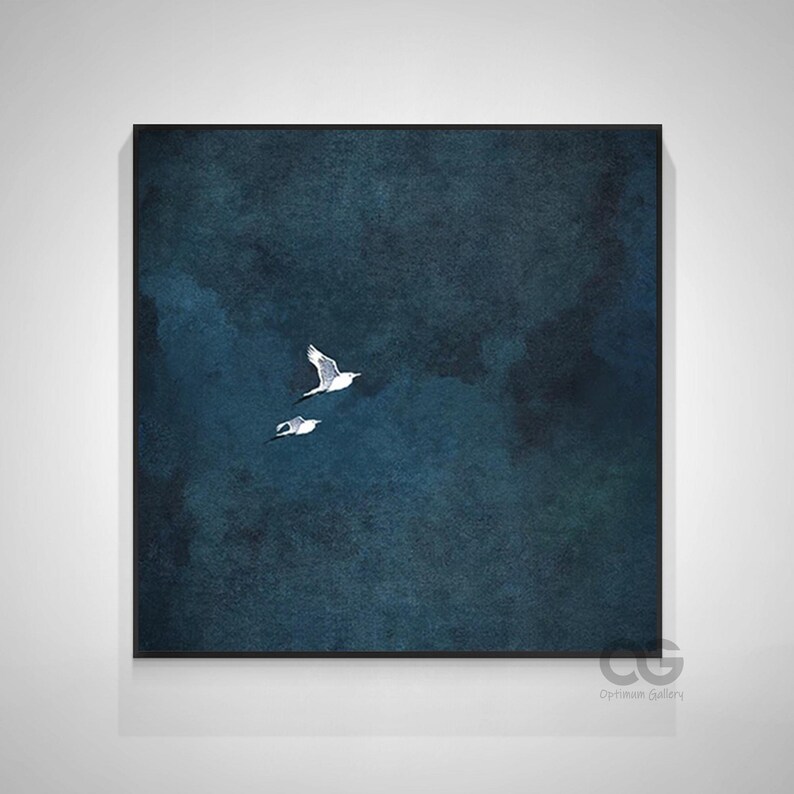 May include: Framed artwork depicting two white seagulls soaring against a dark blue, textured backdrop. The image has a watercolour effect, with subtle variations in the blue tones. The frame is black, and the overall aesthetic is tranquil and calming.