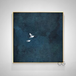 May include: A framed art print depicting two white birds soaring against a dark blue, textured backdrop. The artwork is presented in a gold-coloured frame and is signed in the lower right corner. The theme is nature and flight.