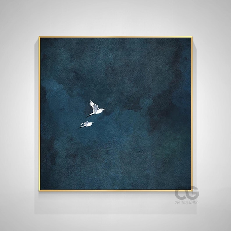 May include: A framed art print depicting two white birds soaring against a dark blue, textured backdrop. The artwork is presented in a gold-coloured frame and is signed in the lower right corner. The theme is nature and flight.