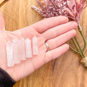 May include: Six clear quartz crystal points, also known as wands, are arranged in a row on a hand. The points are various sizes and are all polished smooth.
