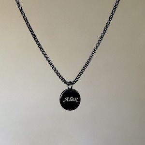 May include: A black chain necklace with a round pendant that says "Alex" in white lettering.