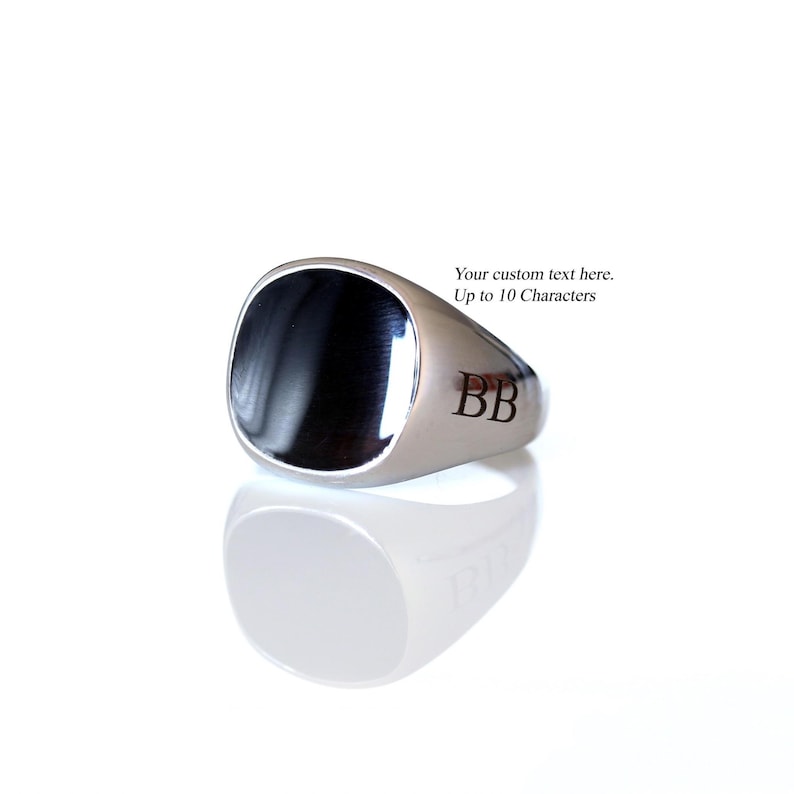May include: A silver-toned signet ring featuring a smooth, polished black inlay on the face and the engraved letters BB on the side. The ring includes text that reads: Your custom text here. Up to 10 Characters.