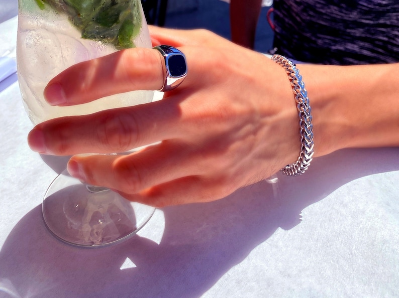 Puede incluir: Un anillo de plata con una piedra negra en el dedo &iacute;ndice de una mano que lleva una pulsera de cadena de plata.