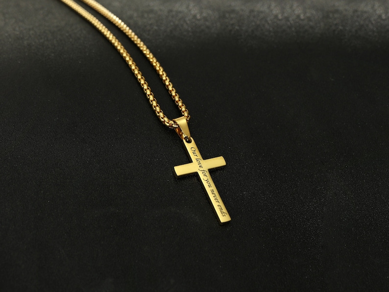 May include: Gold chain necklace with a gold cross pendant. The cross has the inscription "Our love for you never ends".