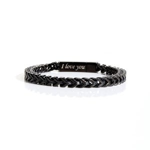 May include: A black metal bracelet featuring a woven chain link design and a rectangular clasp engraved with the text I love you. The bracelet has a dark, polished finish and a structured, repeating pattern throughout the entire band.