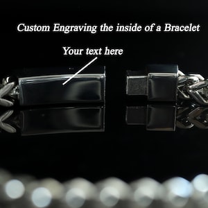Puede incluir: Un brazalete de plata con un cierre que se abre para revelar una superficie plana para grabar. El texto "Your text here" se muestra en la imagen.