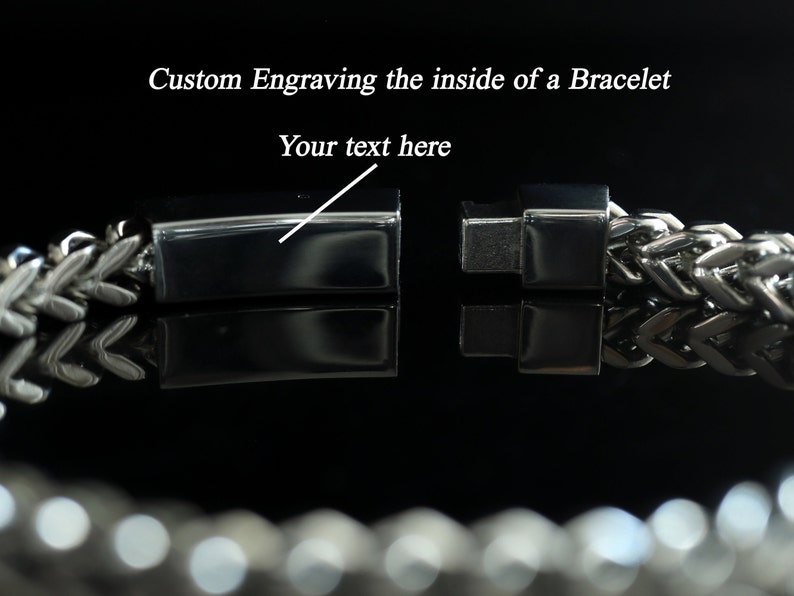 Puede incluir: Un brazalete de plata con un cierre que se abre para revelar una superficie plana para grabar. El texto "Your text here" se muestra en la imagen.