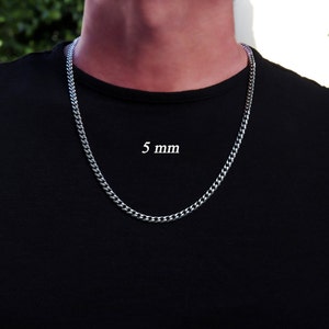 K&ouml;nnte beinhalten: Eine silberne Curb-Kette mit einer Breite von 5 mm. Die Kette wird von einer Person mit einem schwarzen T-Shirt getragen.