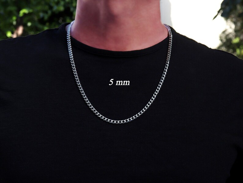K&ouml;nnte beinhalten: Eine silberne Curb-Kette mit einer Breite von 5 mm. Die Kette wird von einer Person mit einem schwarzen T-Shirt getragen.