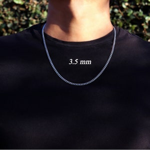 K&ouml;nnte beinhalten: Eine silberne Kettenkette mit einer Breite von 3,5 mm. Die Kette wird von einer Person mit einem schwarzen Shirt getragen.