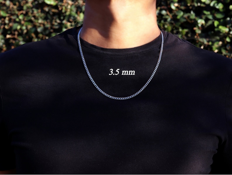 K&ouml;nnte beinhalten: Eine silberne Kettenkette mit einer Breite von 3,5 mm. Die Kette wird von einer Person mit einem schwarzen Shirt getragen.