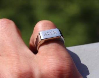 May include: A silver signet ring with the name "ALEX" engraved on the top.