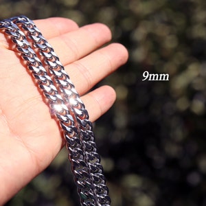 K&ouml;nnte beinhalten: Eine silberne Curb-Kette mit einer Breite von 9 mm. Die Kette wird in einer Hand gezeigt, der Hintergrund ist verschwommen.