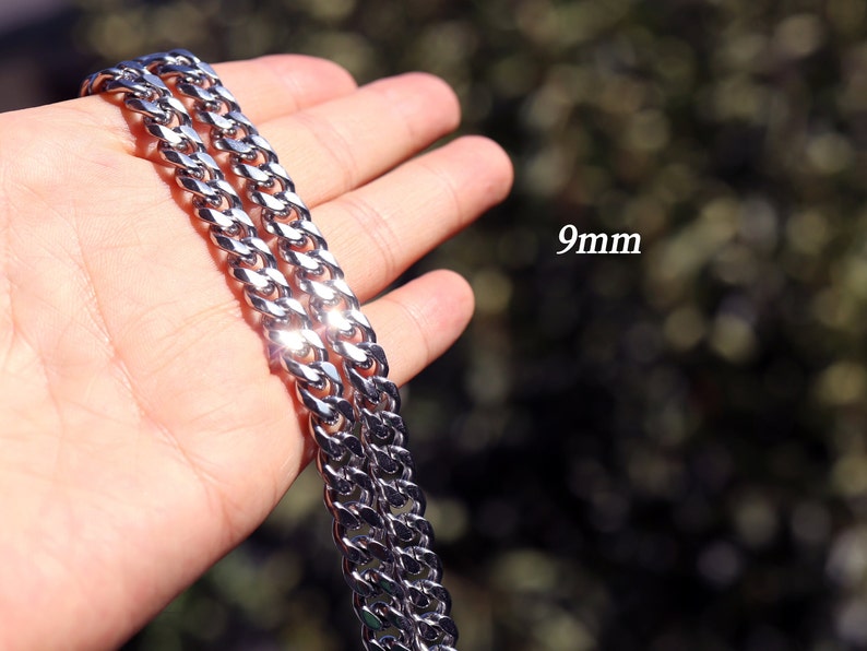 K&ouml;nnte beinhalten: Eine silberne Curb-Kette mit einer Breite von 9 mm. Die Kette wird in einer Hand gezeigt, der Hintergrund ist verschwommen.